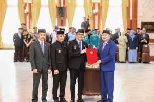 Banjarmasin – Bupati Tanah Bumbu, Andi Rudi Latif, dan Wakil Bupati, H. Bahsanudin, resmi menerima Surat Keputusan (SK) Menteri Dalam Negeri (Mendagri) tentang pengesahan pengangkatan sebagai Bupati dan Wakil Bupati Tanah Bumbu. SK tersebut diserahkan langsung oleh Gubernur Kalimantan Selatan, H. Muhidin, dalam sebuah seremoni di Gedung Mahligai Pancasila, Banjarmasin. (5/3) Selain Tanah Bumbu, kepala daerah dari berbagai kabupaten dan kota di Kalimantan Selatan juga menerima SK pengangkatan dalam kesempatan yang sama. Acara ini menjadi momen penting bagi para kepala daerah yang akan memimpin wilayahnya masing-masing pada periode 2025-2030. Dalam sambutannya, Gubernur H. Muhidin mengingatkan seluruh kepala daerah untuk menjalankan amanah rakyat dengan penuh tanggung jawab. Ia berharap semua pemimpin daerah, termasuk dirinya sebagai Gubernur, diberikan kekuatan dan kemudahan dalam mengemban tugas. “Mudah-mudahan Bupati, Wali Kota, serta para Wakilnya, termasuk saya selaku Gubernur, diberikan kekuatan, kemudahan, dan kelapangan berpikir oleh Allah SWT agar amanah rakyat dapat kita tunaikan dengan sebaik-baiknya,” ujar Muhidin. Gubernur juga menekankan pentingnya peran kepala daerah dalam mendorong program-program yang nyata serta meningkatkan pelayanan kepada masyarakat. “Pesan khusus saya, kepada seluruh kepala daerah, untuk selalu melayani masyarakat dengan baik, jangan mempersulit,” tambahnya. Acara ini turut dihadiri oleh Wakil Gubernur Kalsel, Hasnuryadi Sulaiman, Pj. Sekdaprov Kalsel, M. Syarifuddin, serta jajaran Pimpinan Forkopimda Kalsel. Selain itu, para pengurus PKK se-Kalimantan Selatan juga hadir untuk menyaksikan momen penting tersebut. Selain penyerahan SK, acara ini juga menjadi ajang serah terima memori jabatan bagi para kepala daerah, termasuk di antaranya Andi Rudi Latif – Bahsanudin (Tanah Bumbu), Muhammad Yamin – Ananda (Banjarmasin), Abdul Hadi – Akhmad Fauzi (Balangan), dan lainnya. Sebagai penutup, seluruh kepala daerah yang baru menerima SK pengangkatan berfoto bersama, menandai dimulainya masa kepemimpinan mereka untuk periode 2025-2030.